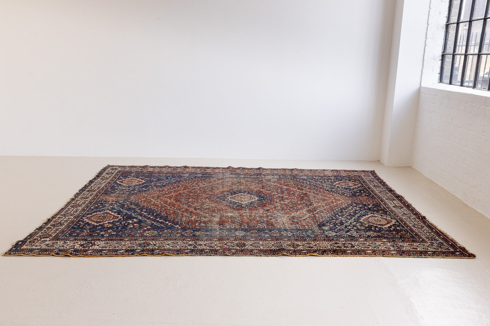 A Qashqai carpet. Sydney features a striking central diamond medallion, a classic motif in Qashqai weaving, framed by a repeating floral, boteh and gul pattern.