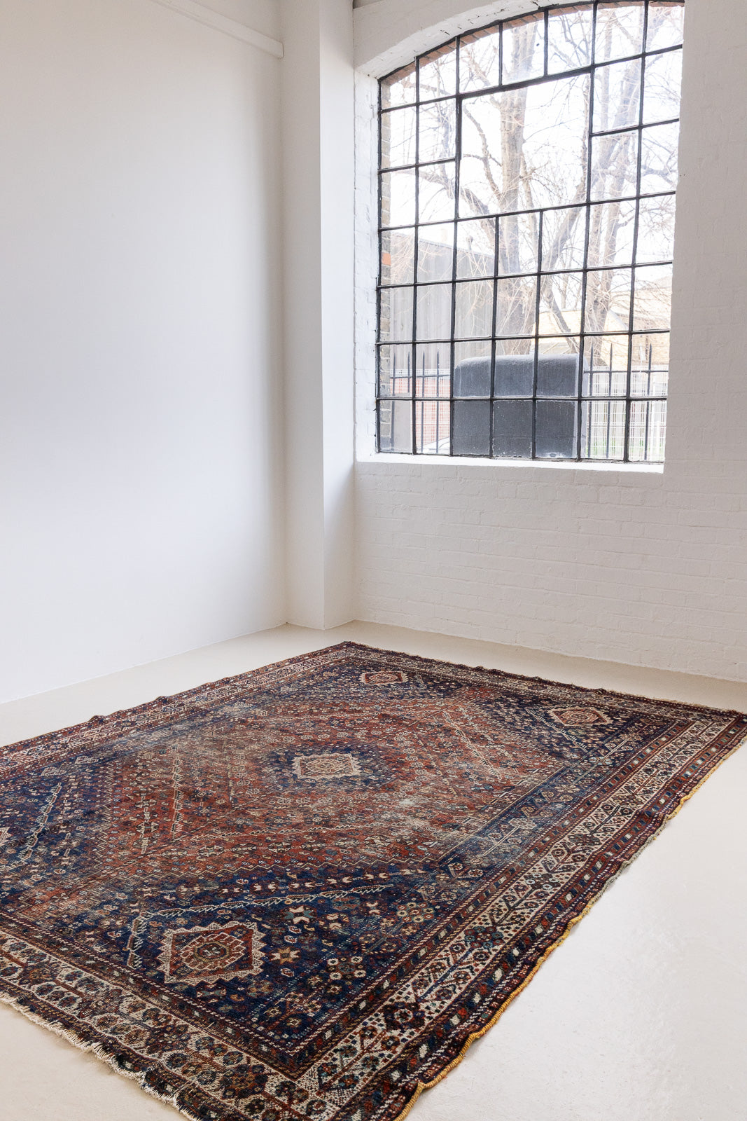 A Qashqai carpet. Sydney features a striking central diamond medallion, a classic motif in Qashqai weaving, framed by a repeating floral, boteh and gul pattern.
