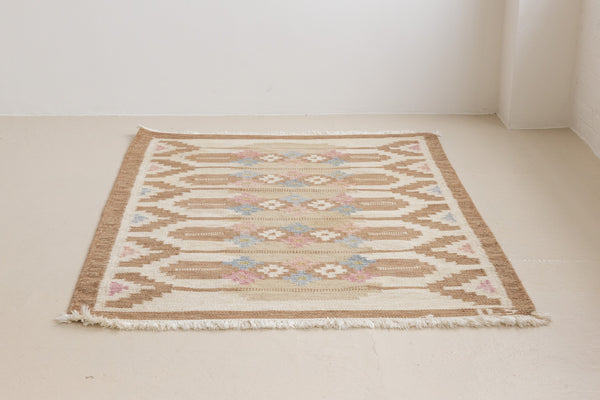 Maja is an original röllakan rug handwoven by the internationally renowned textile designer Ingegerd Silow. This vintage rug features geometric designs in brown, beige, pink and blue on a light beige ground.