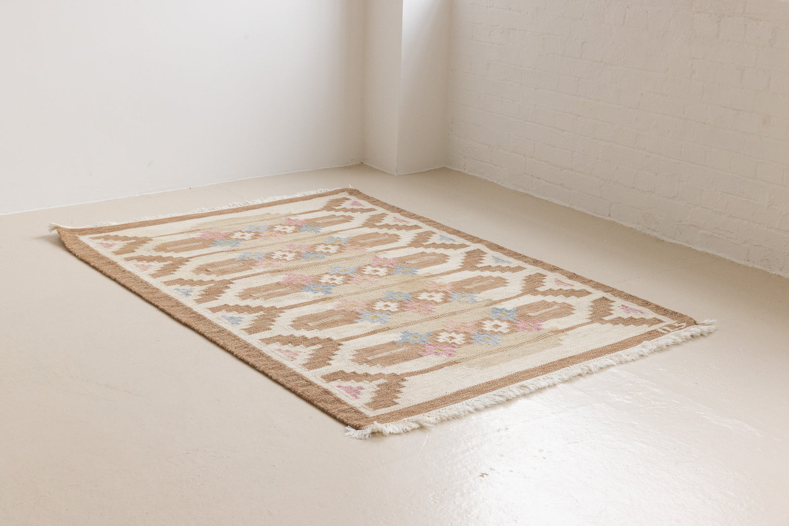 Maja is an original röllakan rug handwoven by the internationally renowned textile designer Ingegerd Silow. This vintage rug features geometric designs in brown, beige, pink and blue on a light beige ground.