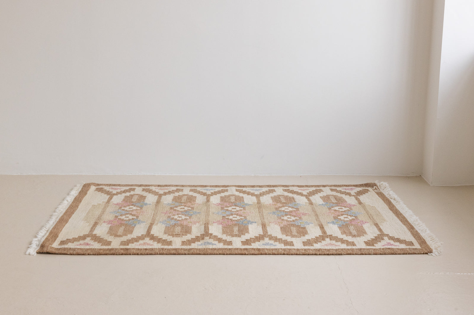 Maja is an original röllakan rug handwoven by the internationally renowned textile designer Ingegerd Silow. This vintage rug features geometric designs in brown, beige, pink and blue on a light beige ground.