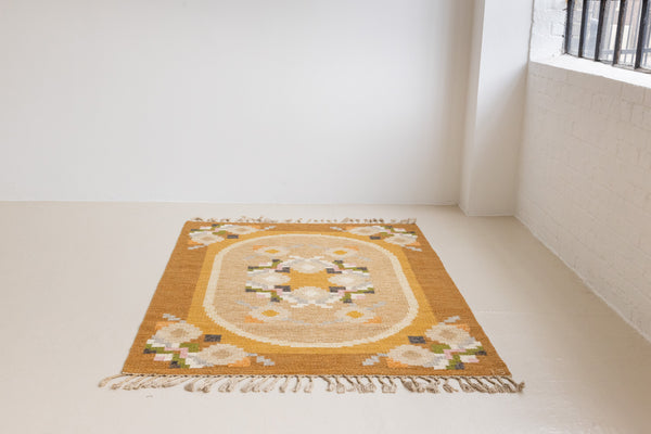 Kaia is a signed vintage Swedish flatweave rug by Ingegerd Silow, featuring a warm ochre field centred framed by stylised florals