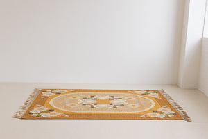 Kaia is a signed vintage Swedish flatweave rug by Ingegerd Silow, featuring a warm ochre field centred framed by stylised florals