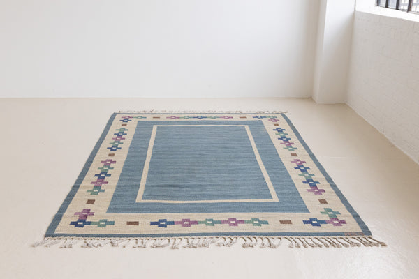 Lumi is a signed vintage Swedish flatweave rug by Anna-Greta Sjöqvist, featuring a calm blue field framed by ivory borders and delicate geometric motifs. Handwoven in wool using the traditional rölakan technique.