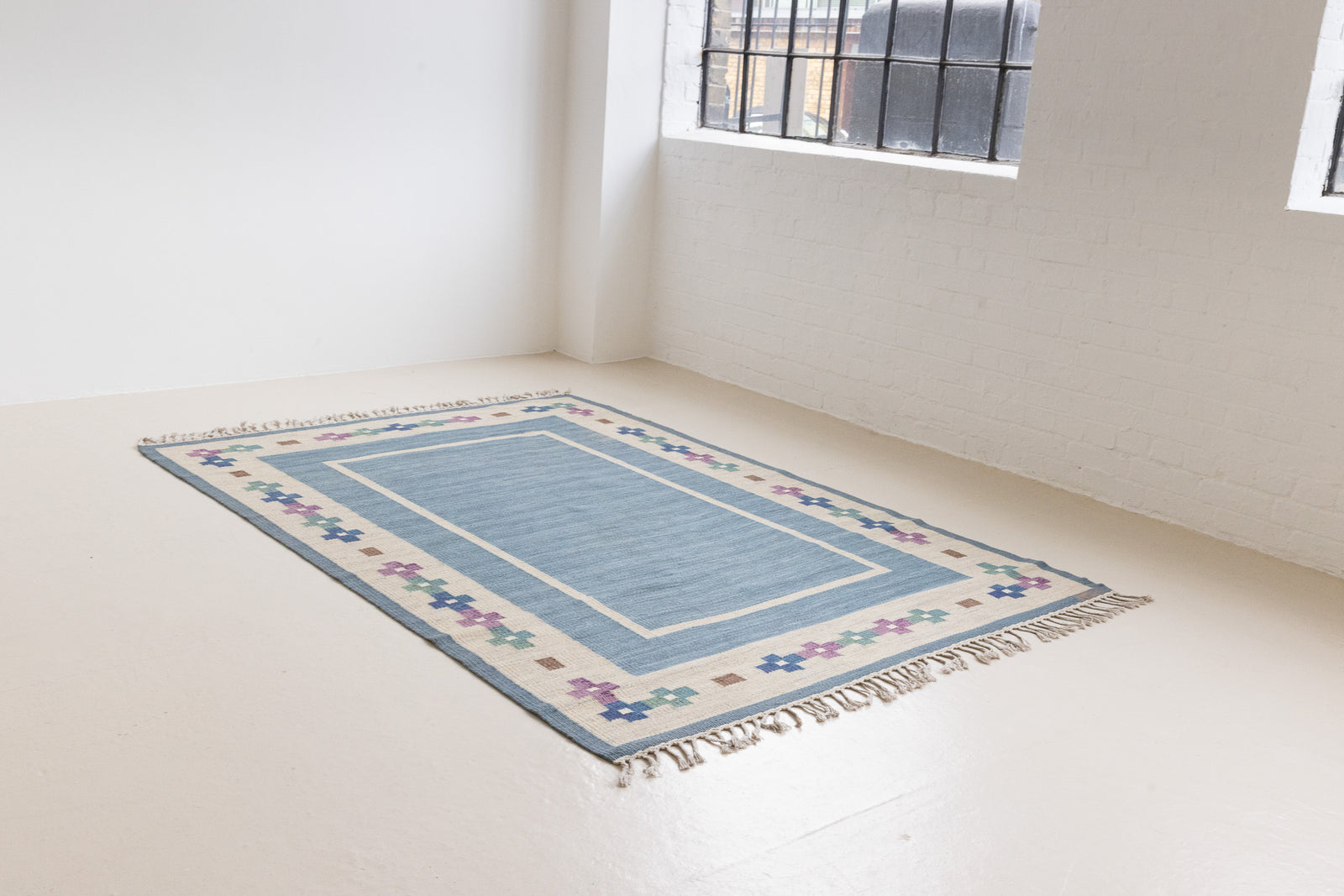 Lumi is a signed vintage Swedish flatweave rug by Anna-Greta Sjöqvist, featuring a calm blue field framed by ivory borders and delicate geometric motifs. Handwoven in wool using the traditional rölakan technique.