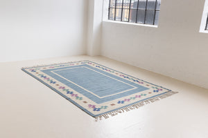 Lumi is a signed vintage Swedish flatweave rug by Anna-Greta Sjöqvist, featuring a calm blue field framed by ivory borders and delicate geometric motifs. Handwoven in wool using the traditional rölakan technique.