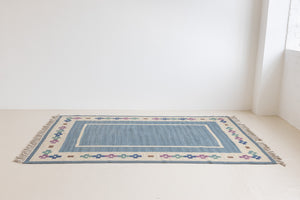 Lumi is a signed vintage Swedish flatweave rug by Anna-Greta Sjöqvist, featuring a calm blue field framed by ivory borders and delicate geometric motifs. Handwoven in wool using the traditional rölakan technique.