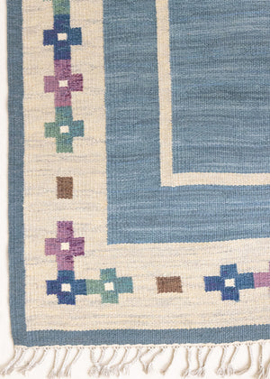 Lumi is a signed vintage Swedish flatweave rug by Anna-Greta Sjöqvist, featuring a calm blue field framed by ivory borders and delicate geometric motifs. Handwoven in wool using the traditional rölakan technique.