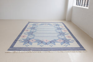 Hallie is an large original röllakan flat weave from the 1960s. This rug shows beautiful tones of blue, featuring bold geometric design with hints of pink within the motifs.