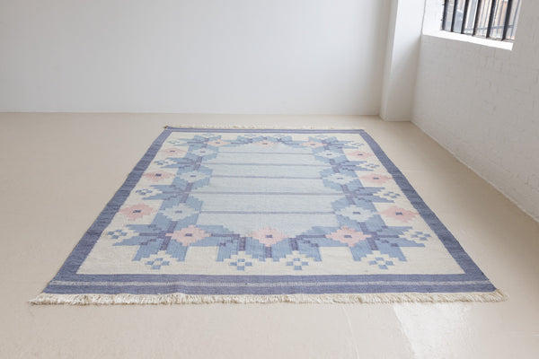 Hallie is an large original röllakan flat weave from the 1960s. This rug shows beautiful tones of blue, featuring bold geometric design with hints of pink within the motifs.
