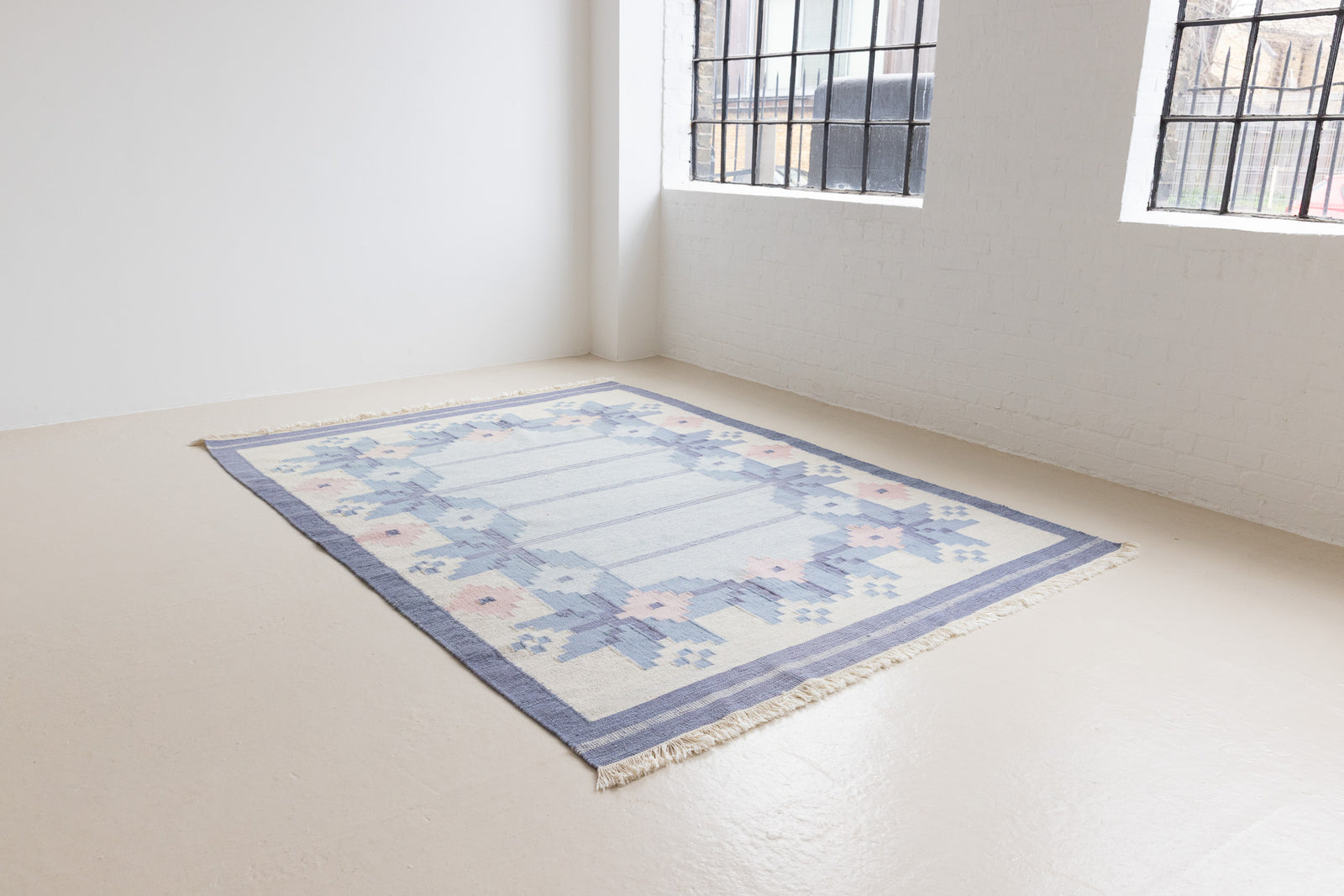 Hallie is an large original röllakan flat weave from the 1960s. This rug shows beautiful tones of blue, featuring bold geometric design with hints of pink within the motifs.
