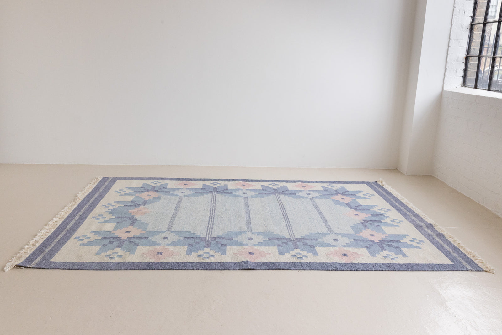 Hallie is an large original röllakan flat weave from the 1960s. This rug shows beautiful tones of blue, featuring bold geometric design with hints of pink within the motifs.
