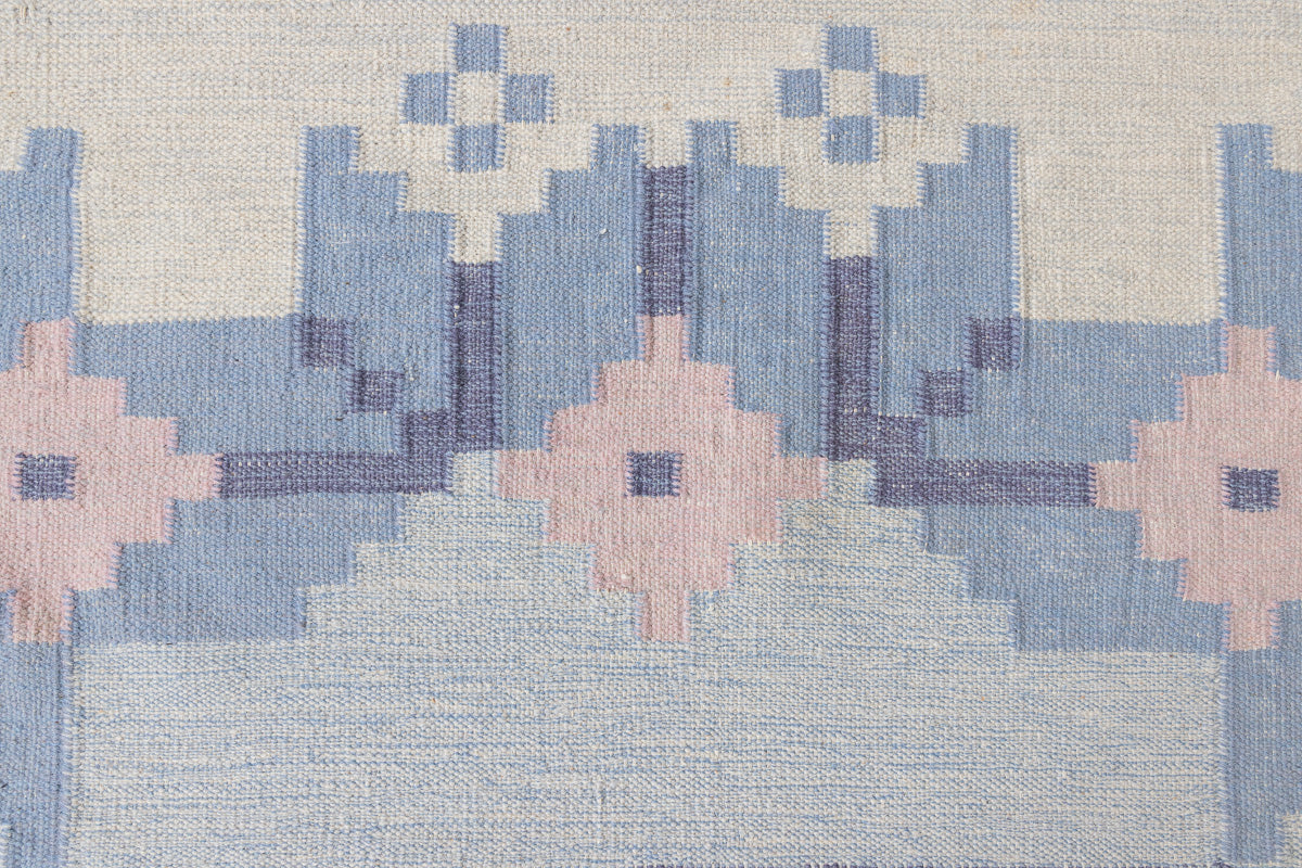 Hallie is an large original röllakan flat weave from the 1960s. This rug shows beautiful tones of blue, featuring bold geometric design with hints of pink within the motifs.
