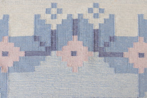 Hallie is an large original röllakan flat weave from the 1960s. This rug shows beautiful tones of blue, featuring bold geometric design with hints of pink within the motifs.
