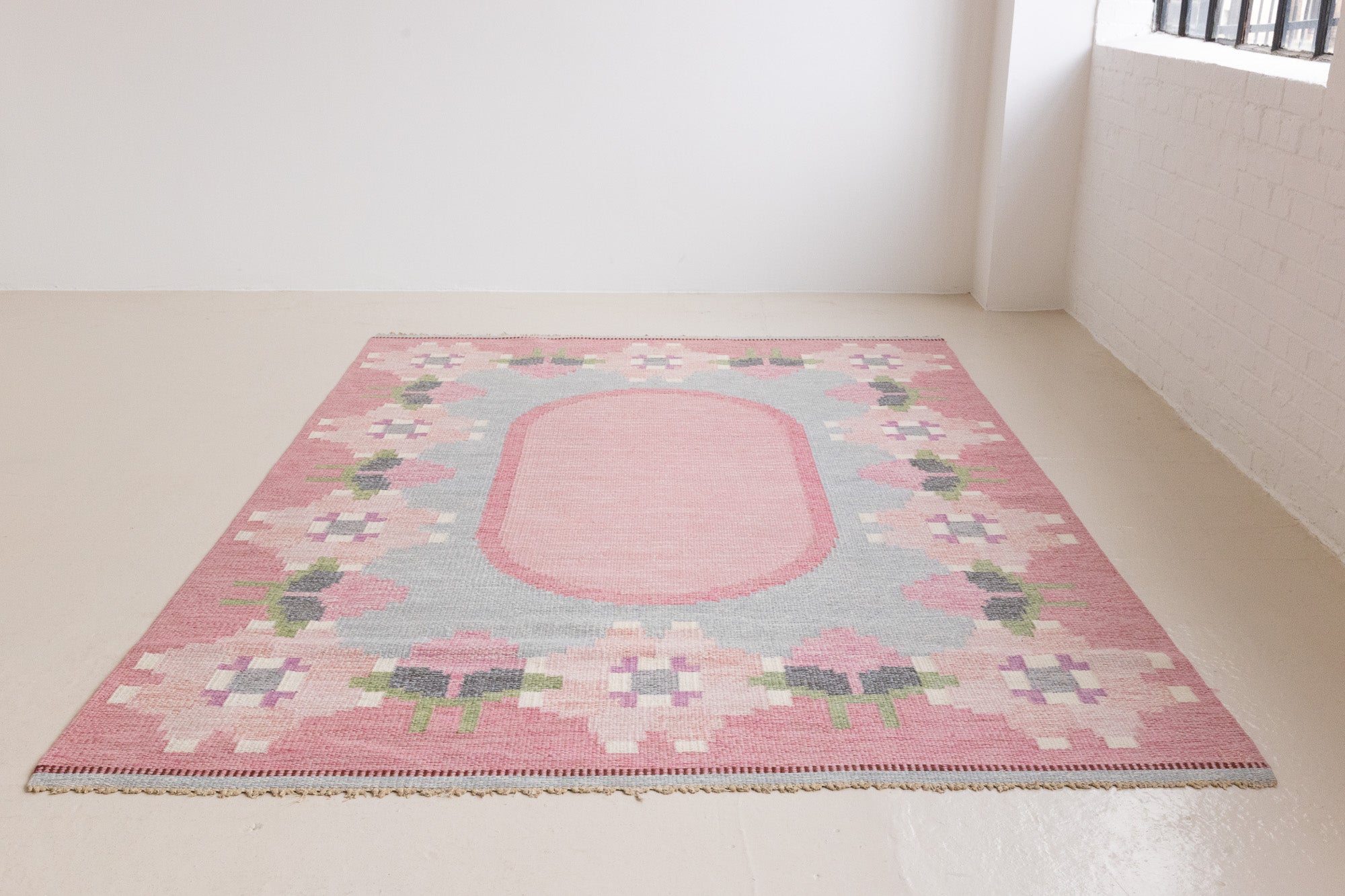 Kara is a vintage Swedish flatweave rug by Ingegerd Silow, featuring a soft pink field, denim blue ground and a pretty and stylised floral border. A leading figure in mid-century Swedish textile design, Silow is known for balancing traditional Nordic craftsmanship with a more decorative, expressive sensibility. This vintage rug features this signature style in its subtle yet playful floral border set against a calm field.
