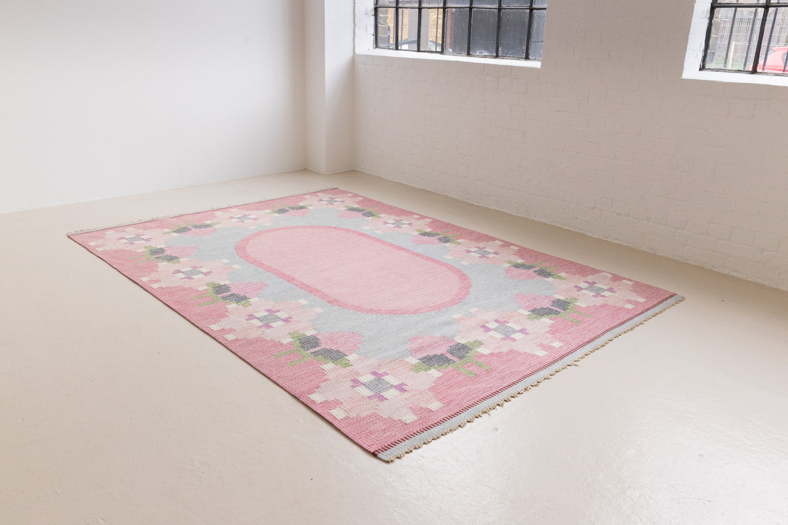 Kara is a vintage Swedish flatweave rug by Ingegerd Silow, featuring a soft pink field, denim blue ground and a pretty and stylised floral border. A leading figure in mid-century Swedish textile design, Silow is known for balancing traditional Nordic craftsmanship with a more decorative, expressive sensibility. This vintage rug features this signature style in its subtle yet playful floral border set against a calm field.