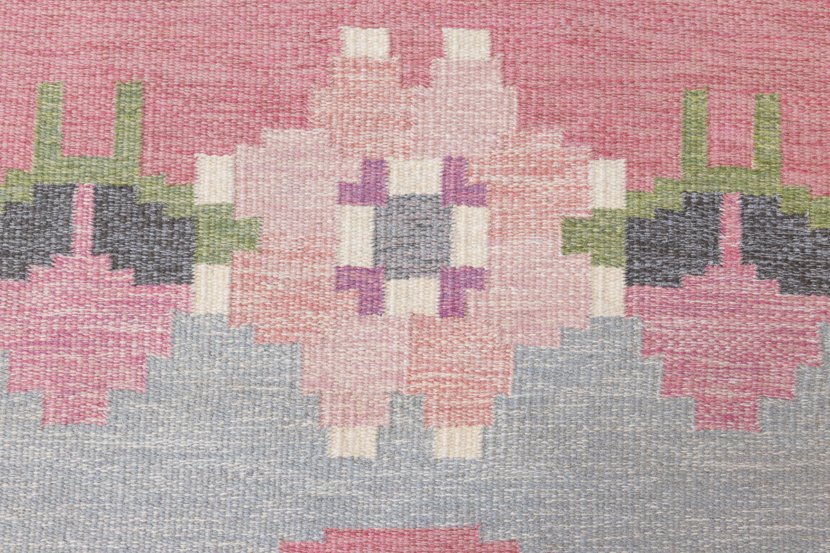 Kara is a vintage Swedish flatweave rug by Ingegerd Silow, featuring a soft pink field, denim blue ground and a pretty and stylised floral border. A leading figure in mid-century Swedish textile design, Silow is known for balancing traditional Nordic craftsmanship with a more decorative, expressive sensibility. This vintage rug features this signature style in its subtle yet playful floral border set against a calm field.