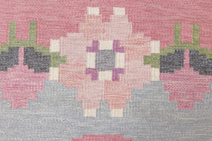 Kara is a vintage Swedish flatweave rug by Ingegerd Silow, featuring a soft pink field, denim blue ground and a pretty and stylised floral border. A leading figure in mid-century Swedish textile design, Silow is known for balancing traditional Nordic craftsmanship with a more decorative, expressive sensibility. This vintage rug features this signature style in its subtle yet playful floral border set against a calm field.
