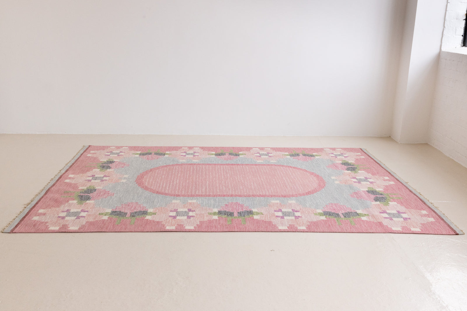 Kara is a vintage Swedish flatweave rug by Ingegerd Silow, featuring a soft pink field, denim blue ground and a pretty and stylised floral border. A leading figure in mid-century Swedish textile design, Silow is known for balancing traditional Nordic craftsmanship with a more decorative, expressive sensibility. This vintage rug features this signature style in its subtle yet playful floral border set against a calm field.