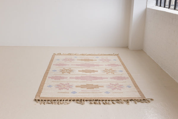 Trina is an original Swedish röllakan rug handwoven by the mid-century textile designer Anna Johanna Angström. This vintage rug features geometric designs in pink, blue, and brown on a beige ground.