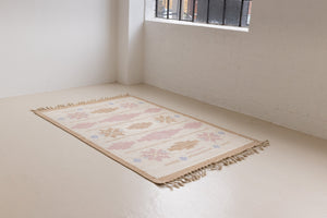 Trina is an original Swedish röllakan rug handwoven by the mid-century textile designer Anna Johanna Angström. This vintage rug features geometric designs in pink, blue, and brown on a beige ground.