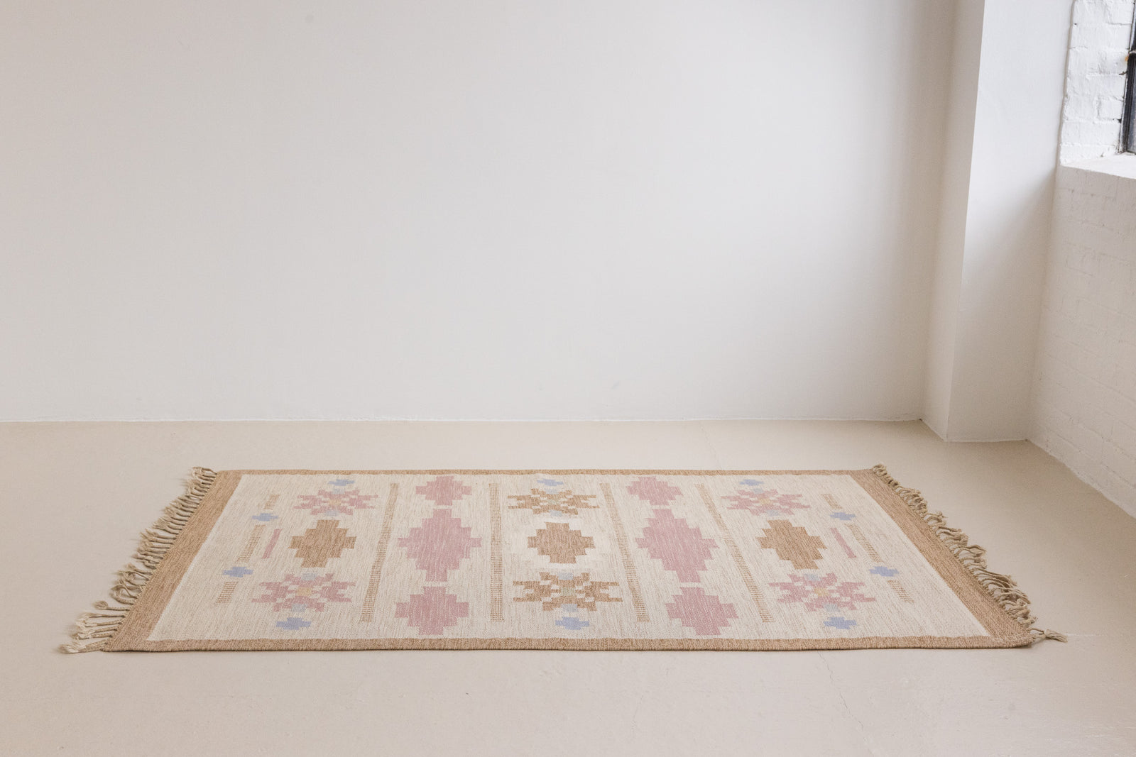 Trina is an original Swedish röllakan rug handwoven by the mid-century textile designer Anna Johanna Angström. This vintage rug features geometric designs in pink, blue, and brown on a beige ground.
