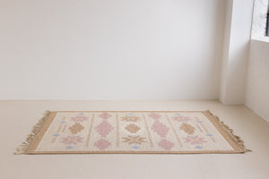 Trina is an original Swedish röllakan rug handwoven by the mid-century textile designer Anna Johanna Angström. This vintage rug features geometric designs in pink, blue, and brown on a beige ground.