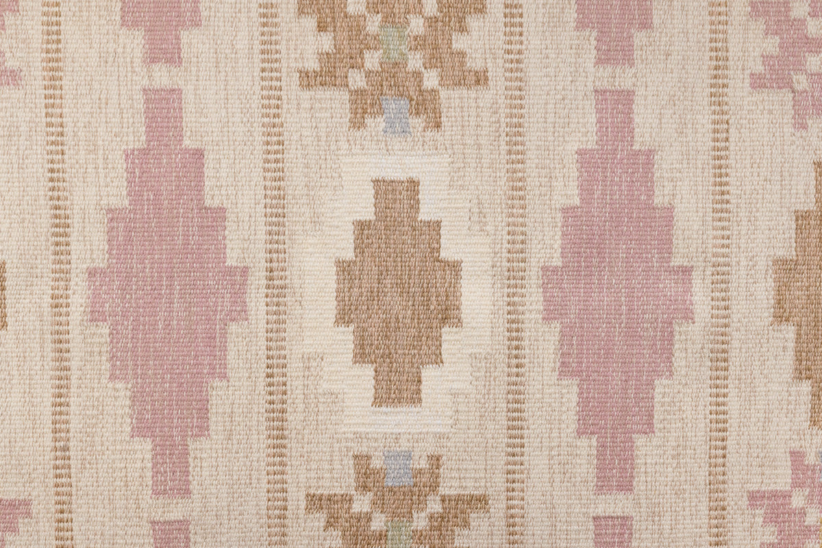 Trina is an original Swedish röllakan rug handwoven by the mid-century textile designer Anna Johanna Angström. This vintage rug features geometric designs in pink, blue, and brown on a beige ground.