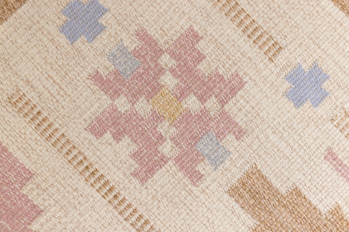Trina is an original Swedish röllakan rug handwoven by the mid-century textile designer Anna Johanna Angström. This vintage rug features geometric designs in pink, blue, and brown on a beige ground.