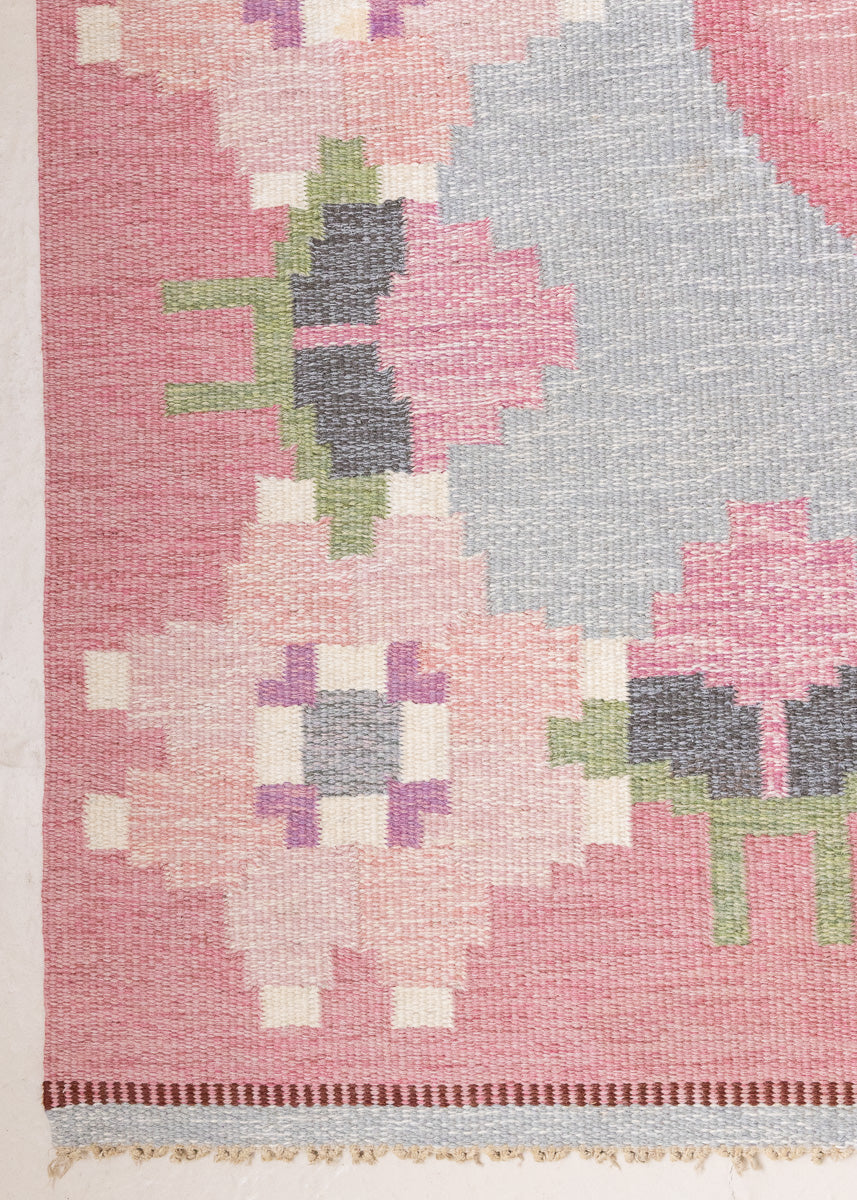 Kara is a vintage Swedish flatweave rug by Ingegerd Silow, featuring a soft pink field, denim blue ground and a pretty and stylised floral border. A leading figure in mid-century Swedish textile design, Silow is known for balancing traditional Nordic craftsmanship with a more decorative, expressive sensibility. This vintage rug features this signature style in its subtle yet playful floral border set against a calm field.