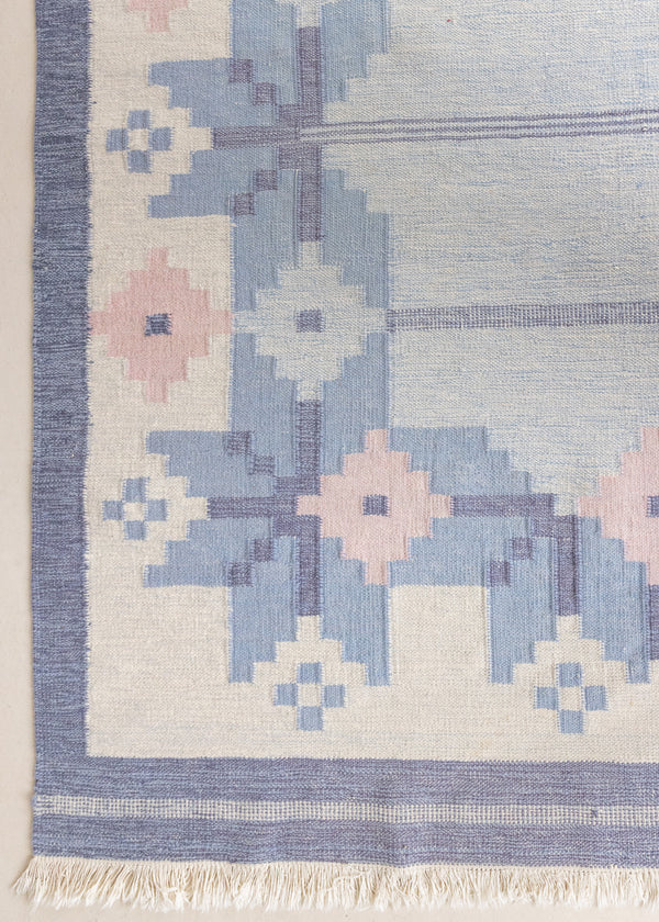 Hallie is an large original röllakan flat weave from the 1960s. This rug shows beautiful tones of blue, featuring bold geometric design with hints of pink within the motifs.
