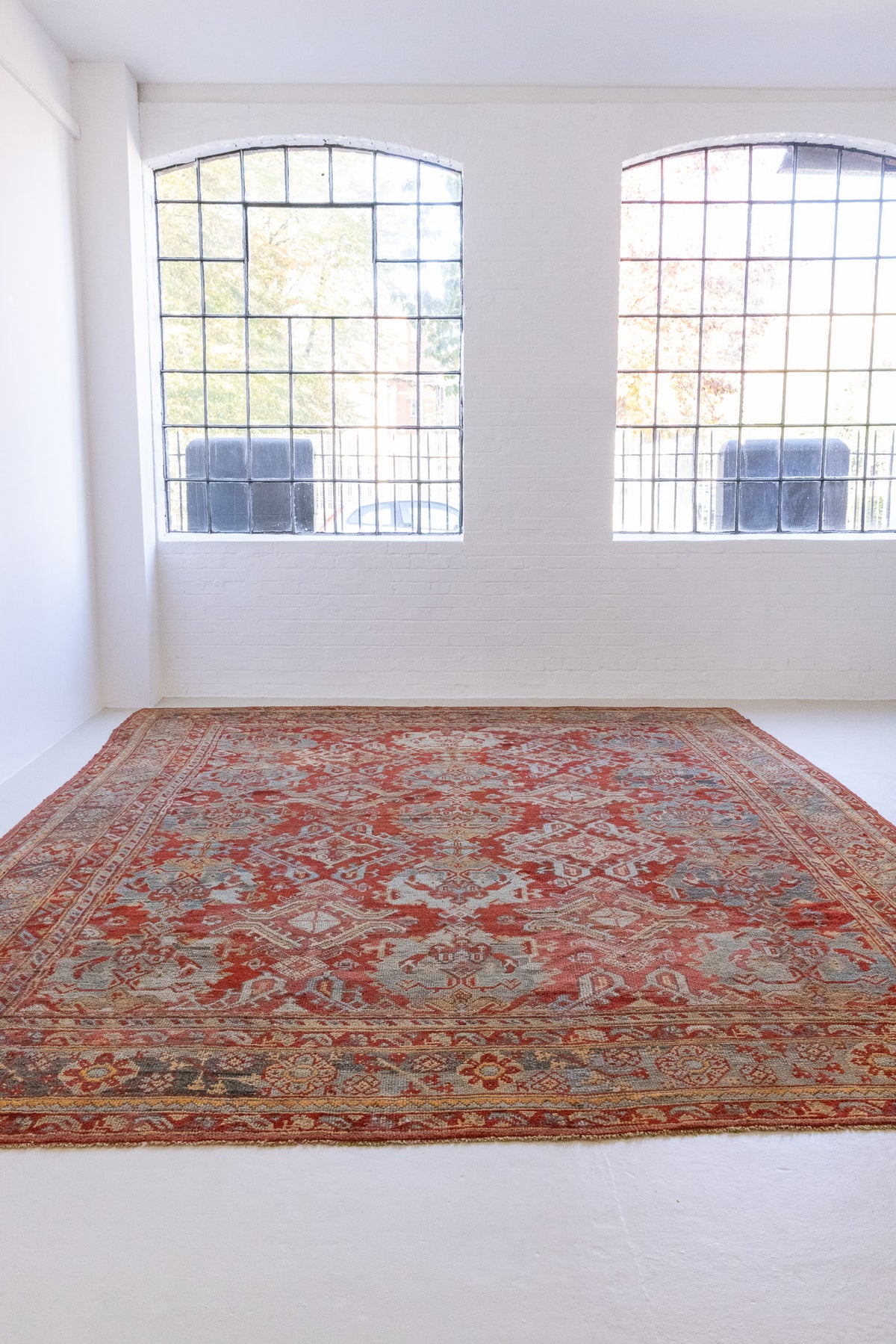 Handwoven antique Oushak carpet with a red field and an intricate decorative design in blue