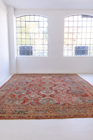 Handwoven antique Oushak carpet with a red field and an intricate decorative design in blue