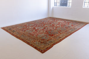 Handwoven antique Oushak carpet with a red field and an intricate decorative design in blue