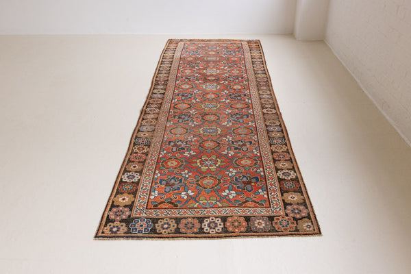 Handwoven antique Persian carpet runner with a rust field and an intricate all-over floral pattern