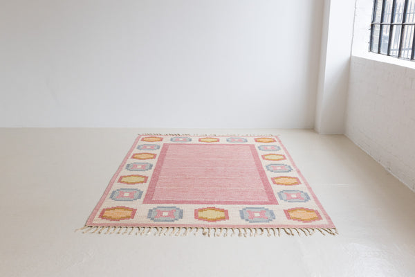 A Vintage Swedish Rug by Ingegerd Silow. An original röllakan flatweave carpet featuring a pink field and unique geometric design. 