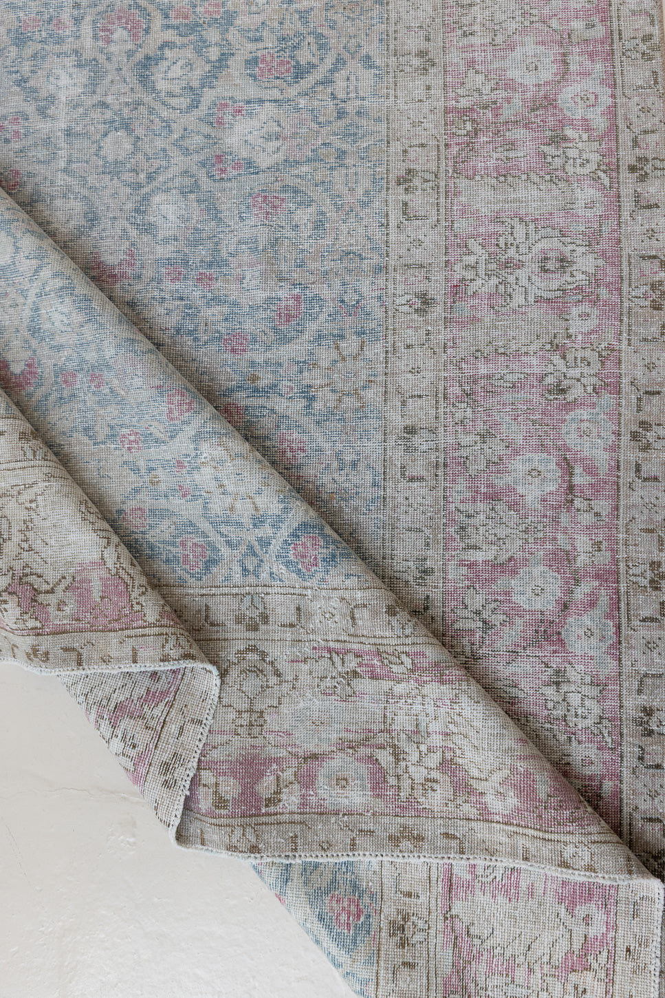 This is an antique Persian Tabriz handwoven carpet in muted blue and pinky red with ivory tones. This vintage hand woven wool rug features a all over floral design.