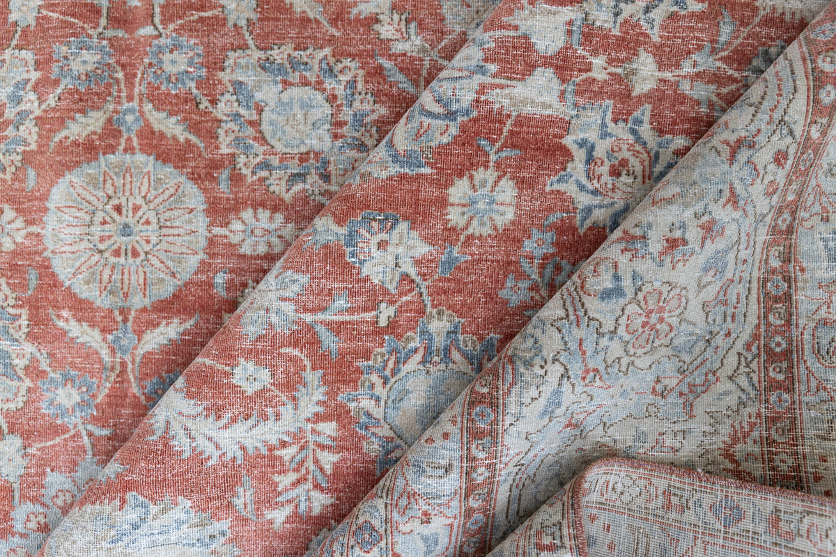 This is an antique Persian Kashan handwoven carpet in blue red and ivory tones. This hand woven antique wool rug features a all over floral design.