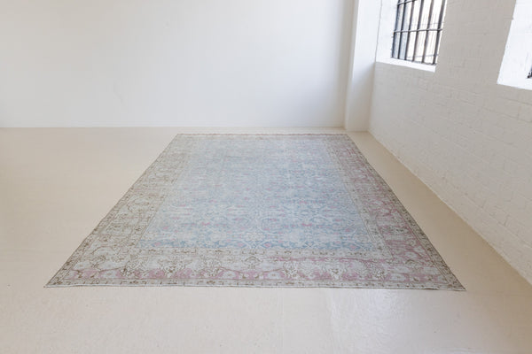 This is an antique Persian Tabriz handwoven carpet in muted blue and pinky red with ivory tones. This vintage hand woven wool rug features a all over floral design.