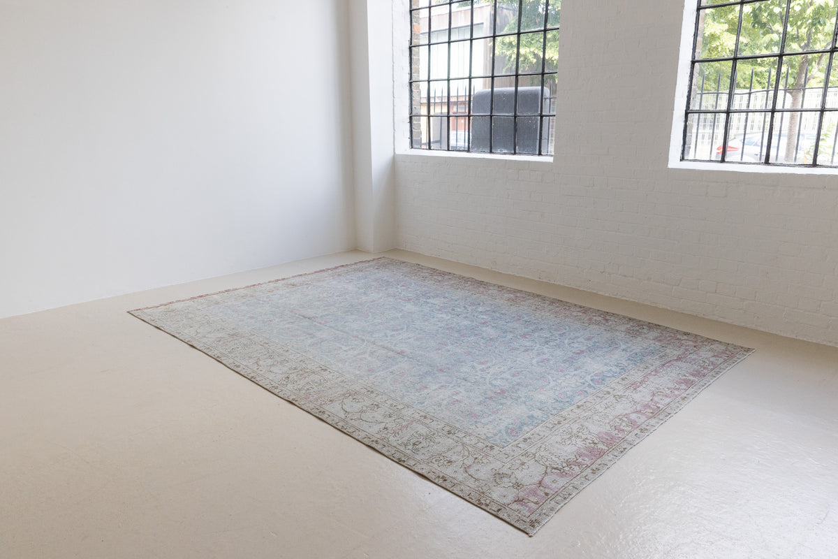 This is an antique Persian Tabriz handwoven carpet in muted blue and pinky red with ivory tones. This vintage hand woven wool rug features a all over floral design.