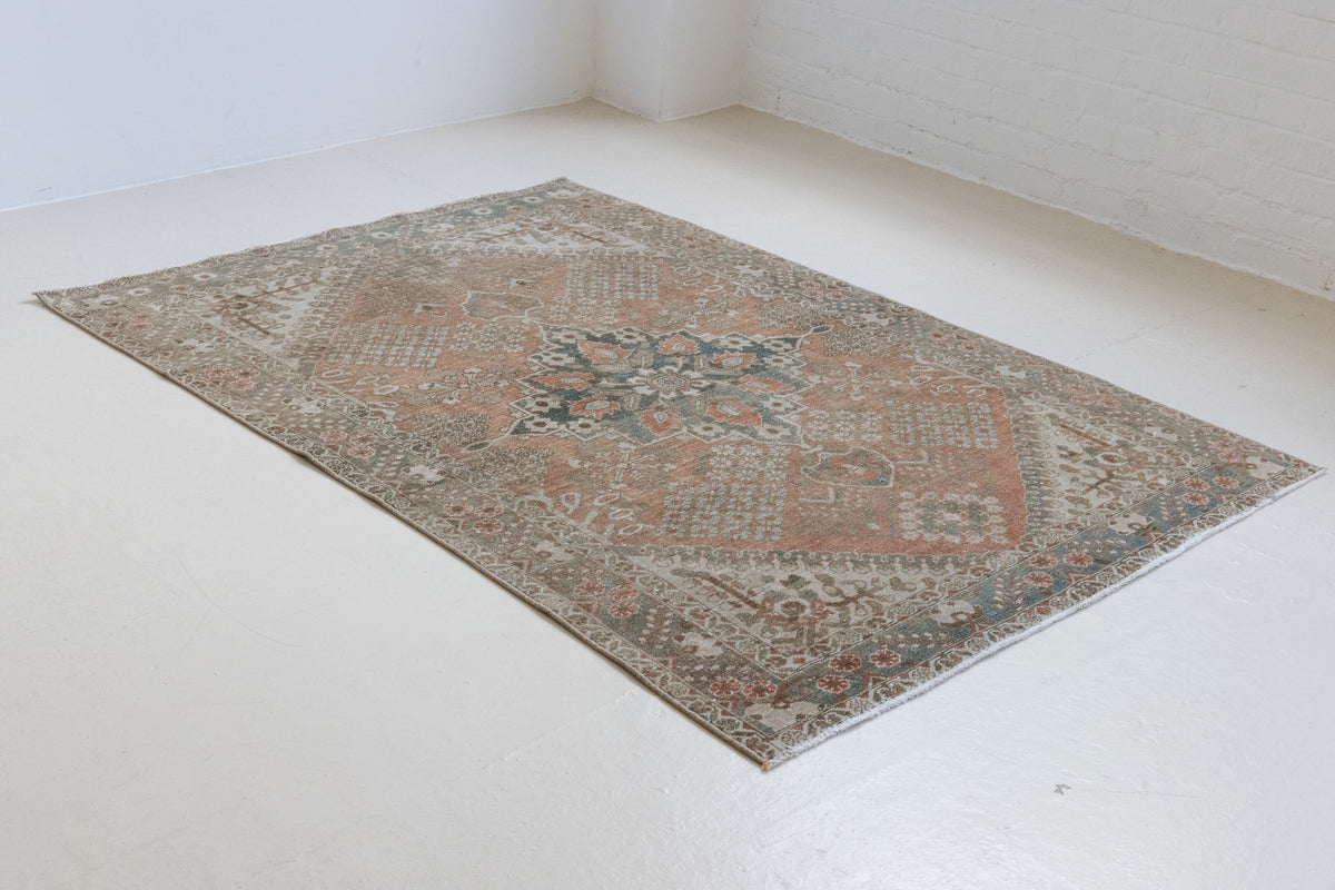 An antique Persian Bakhtiyari rug with a bold medallion in blue, green and terracotta. This handwoven Persian carpet boasts a  pretty floral border.