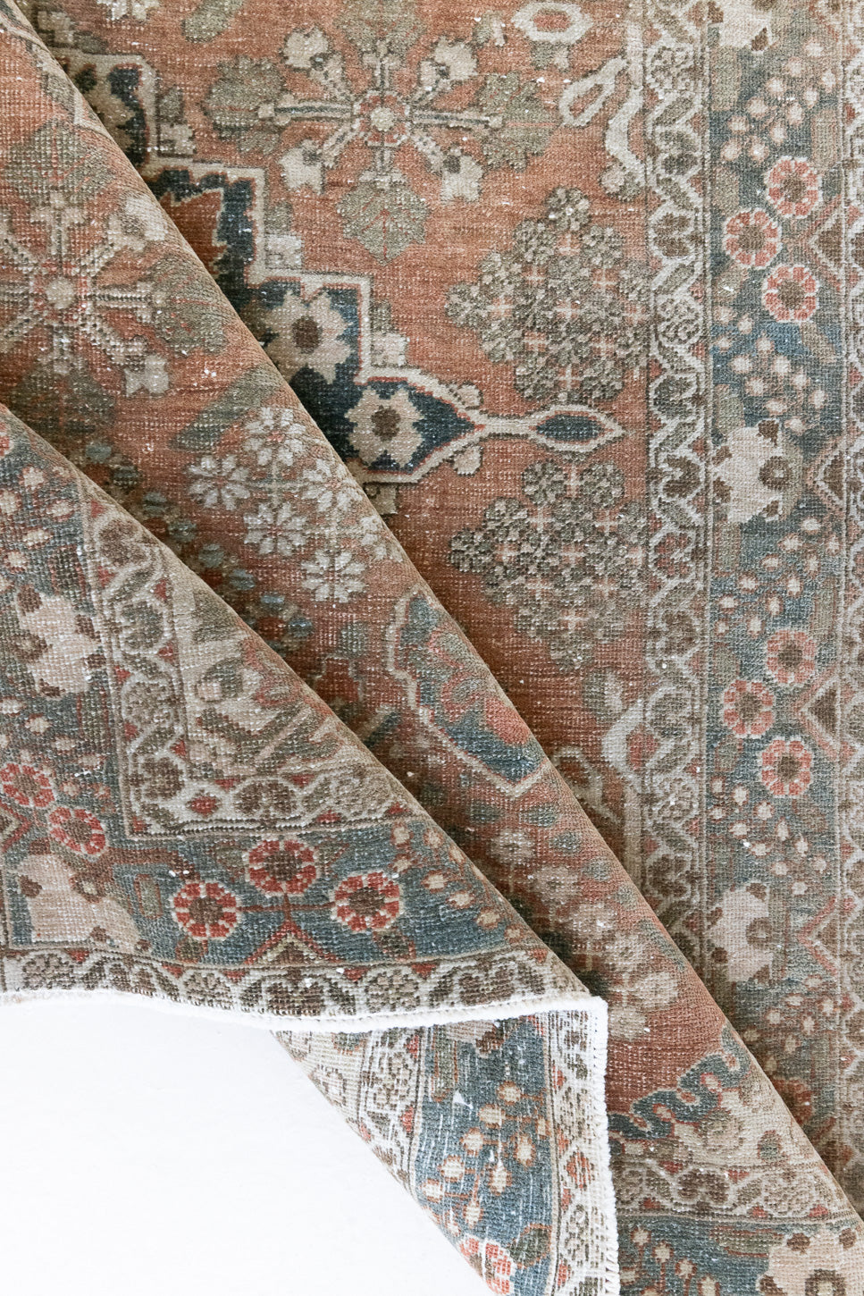 A close up of an antique Persian Bakhtiyari rug with a bold medallion in blue, green and terracotta. This handwoven Persian carpet has a lovely design and a floral border.