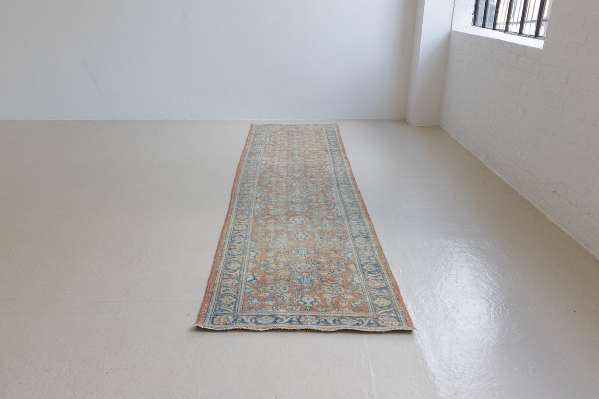 This is an large antique Persian Mahal runner handwoven carpet in a rusty orange red  and muted blue with ivory tones. This vintage hand woven wool rug features a all over floral design.