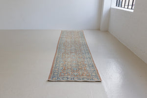 This is an large antique Persian Mahal runner handwoven carpet in a rusty orange red  and muted blue with ivory tones. This vintage hand woven wool rug features a all over floral design.