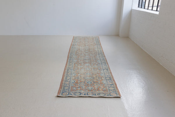 This is an large antique Persian Mahal runner handwoven carpet in a rusty orange red  and muted blue with ivory tones. This vintage hand woven wool rug features a all over floral design.
