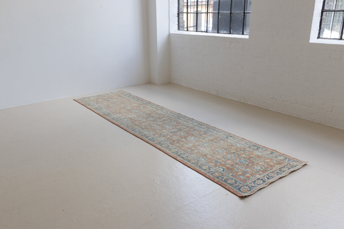 This is an large antique Persian Mahal runner handwoven carpet in a rusty orange red  and muted blue with ivory tones. This vintage hand woven wool rug features a all over floral design.