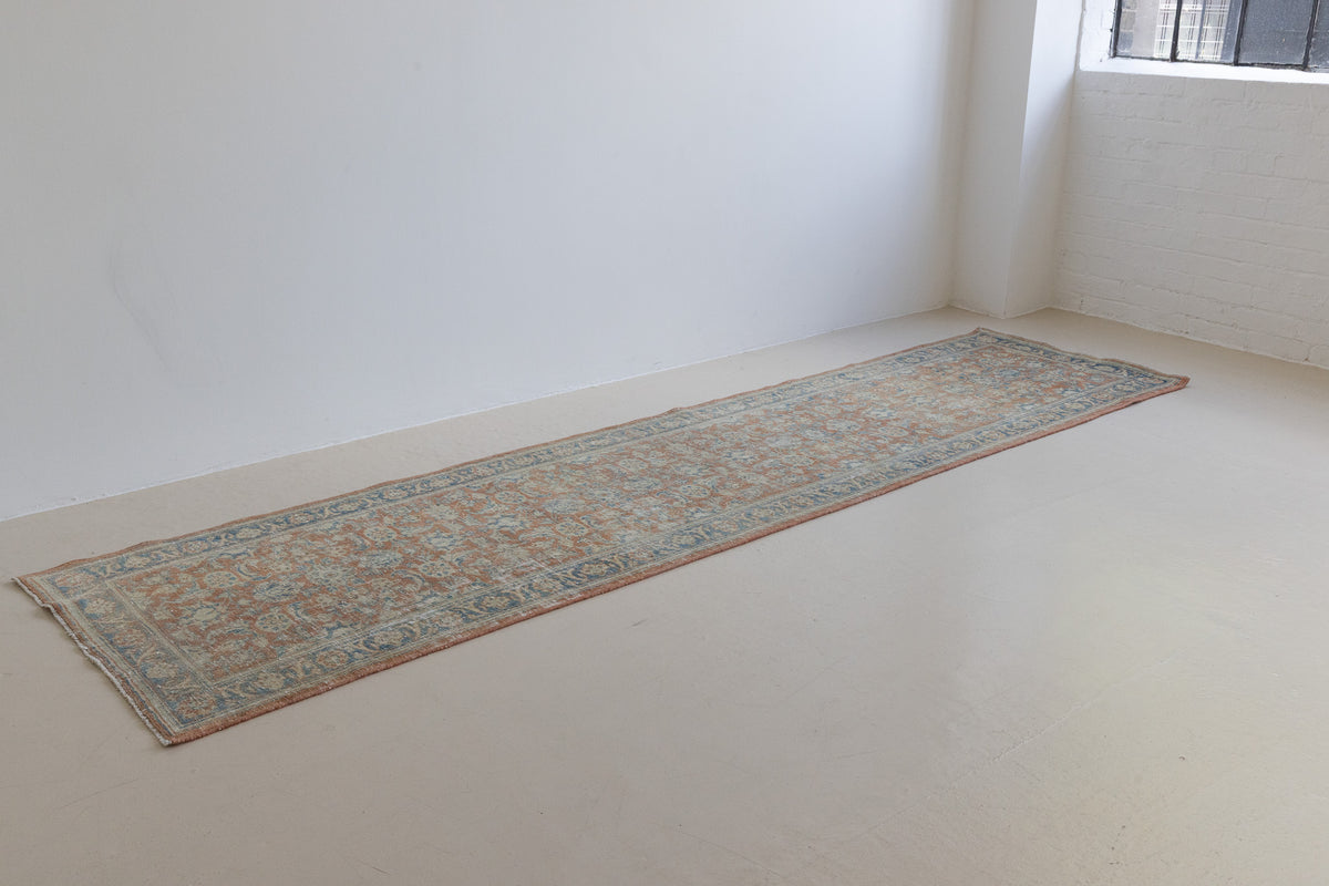 This is an large antique Persian Mahal runner handwoven carpet in a rusty orange red  and muted blue with ivory tones. This vintage hand woven wool rug features a all over floral design.