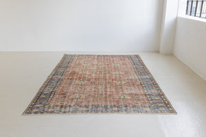 This is an large antique Turkish handwoven carpet in a rusty orange red  and muted blue with ivory tones. This vintage hand woven wool rug features a all over floral design.