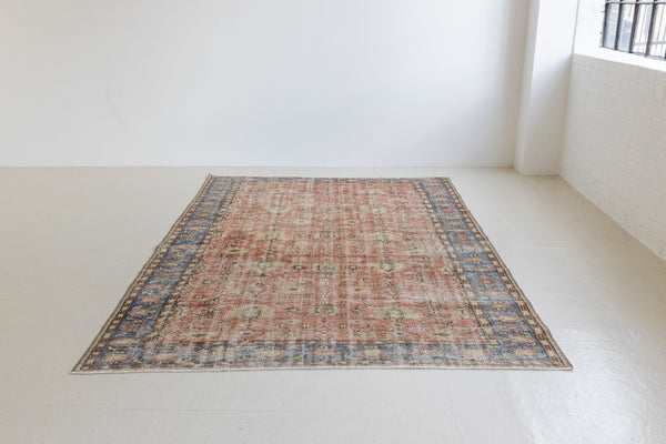 This is an large antique Turkish handwoven carpet in a rusty orange red  and muted blue with ivory tones. This vintage hand woven wool rug features a all over floral design.