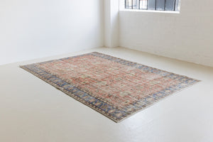 This is an large antique Turkish handwoven carpet in a rusty orange red  and muted blue with ivory tones. This vintage hand woven wool rug features a all over floral design.